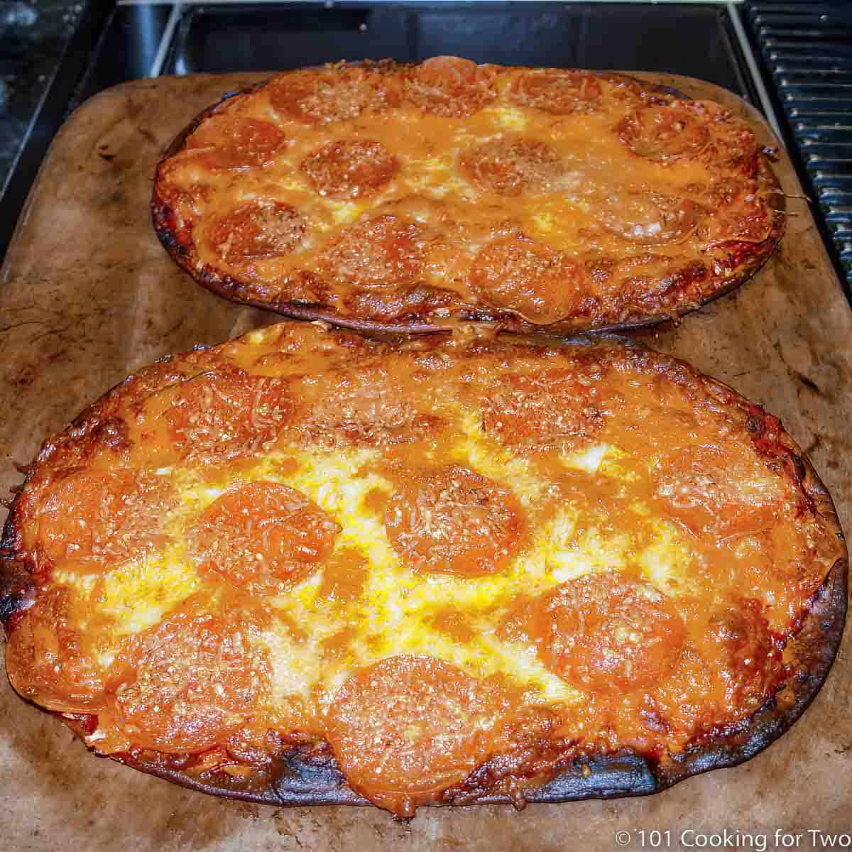 Two cooked flat bread pizzas on a stone