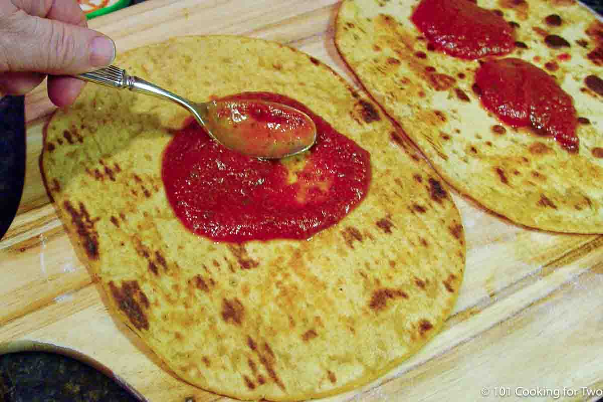 spreading sauce on browned tortilla.