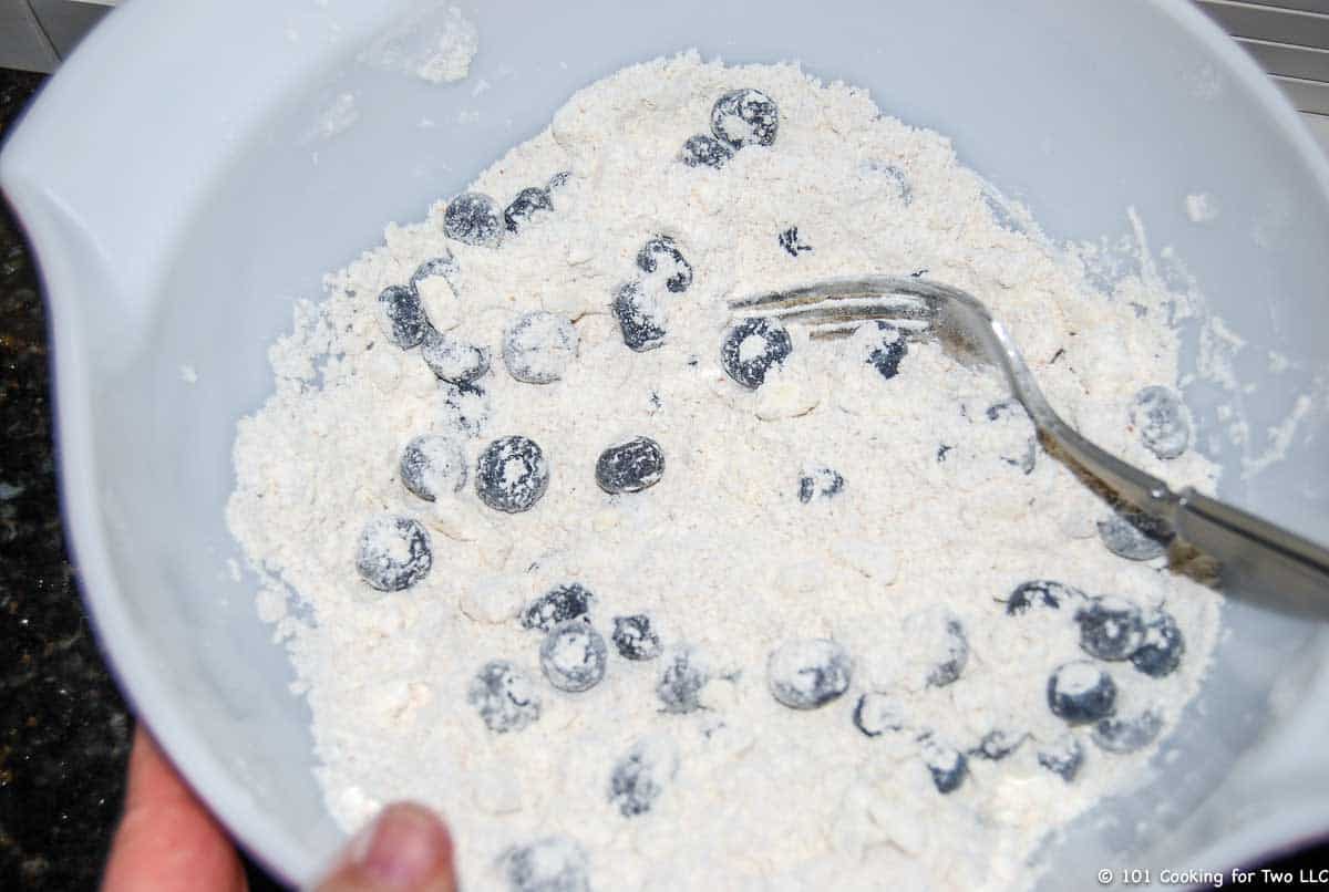 adding blueberries into bowl of flour.