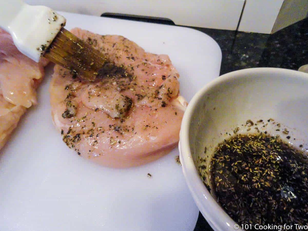 brushing chicken breast with seasoning on white board