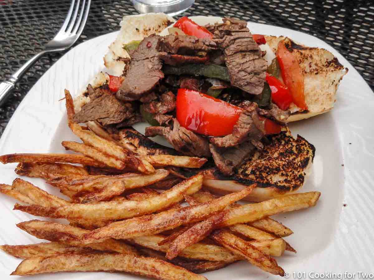 Philly sandwich on plate with fries.