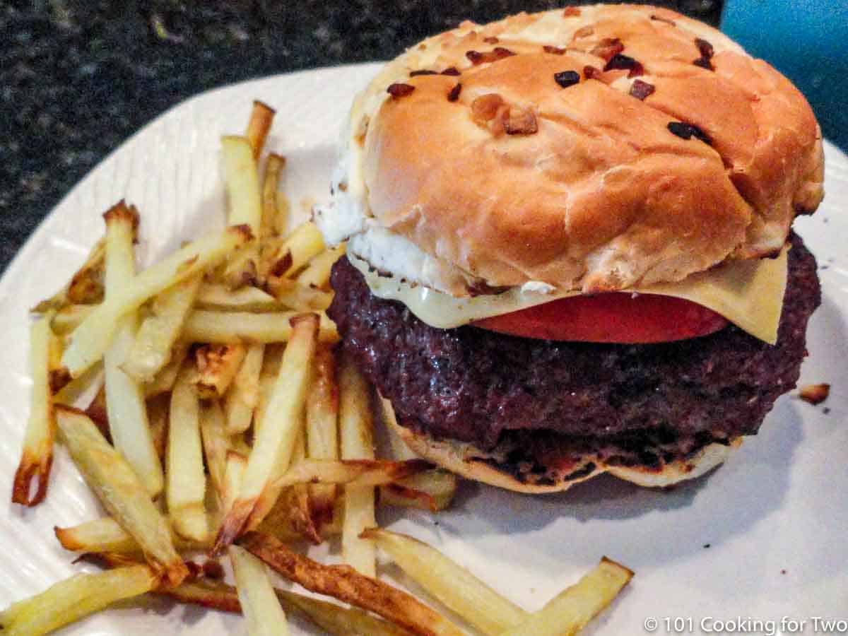 burger in bun with fries on white plate