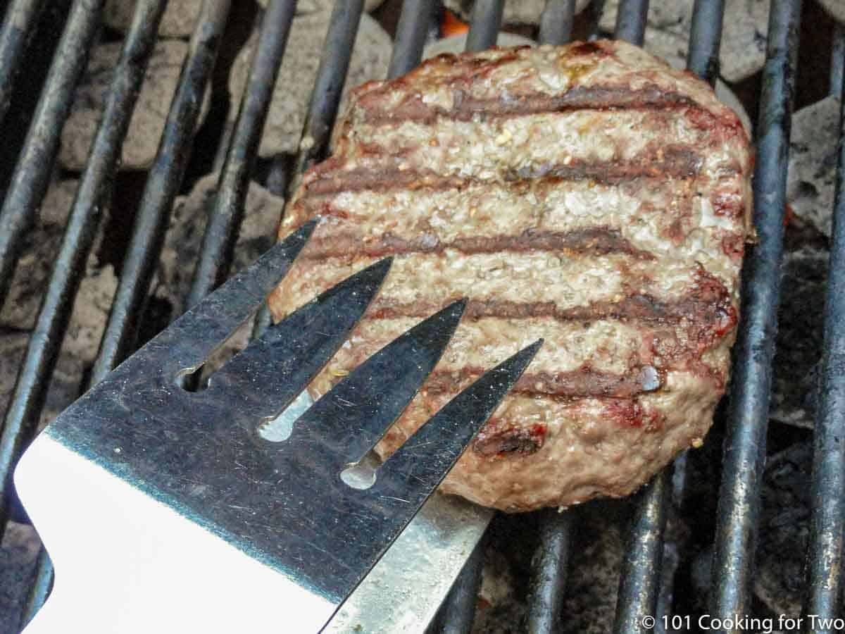 flipping a partly cooked burger on the grill
