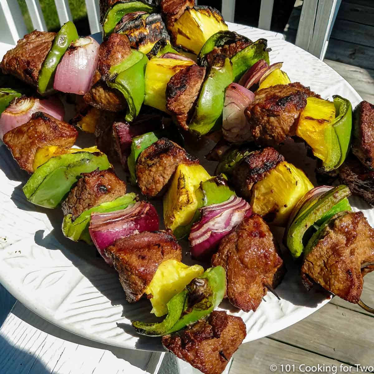 a pile of done beef and veggie kabobs on a white plate