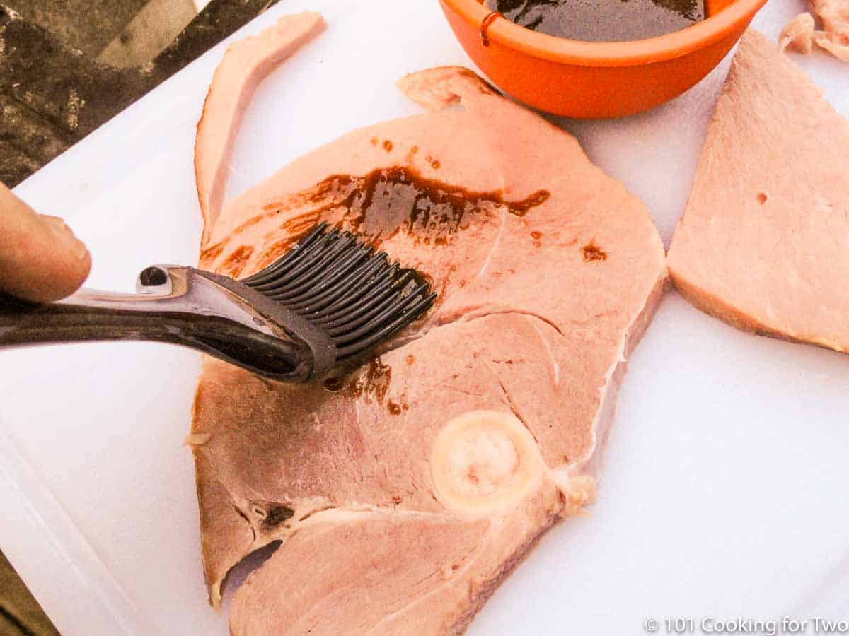 brushing the ham with the glaze on a white board.