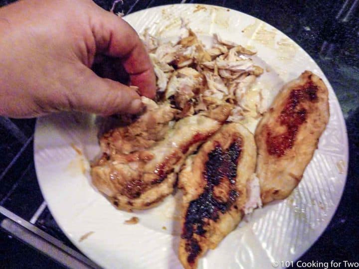 hand shredding chicken on plate