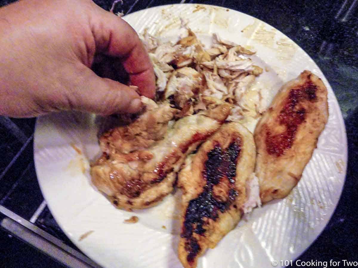 hand shredding chicken on plate.