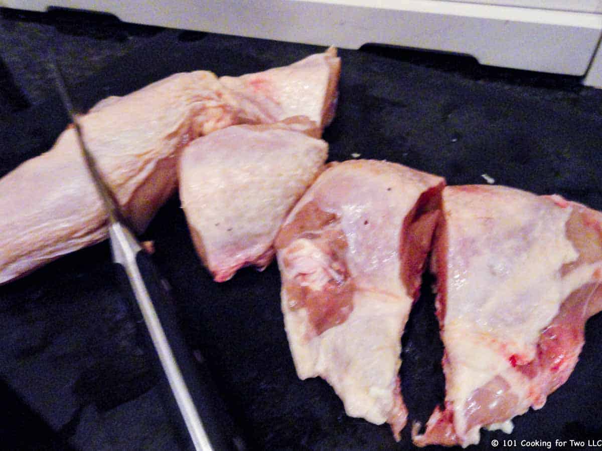 Cutting cut chicken breasts in half on board.