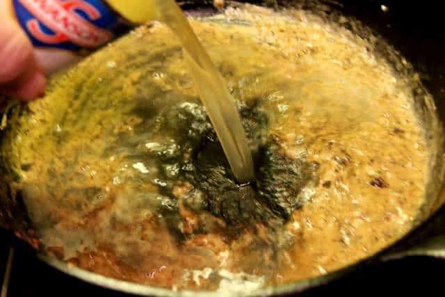 image of adding broth to the roux in a black pan