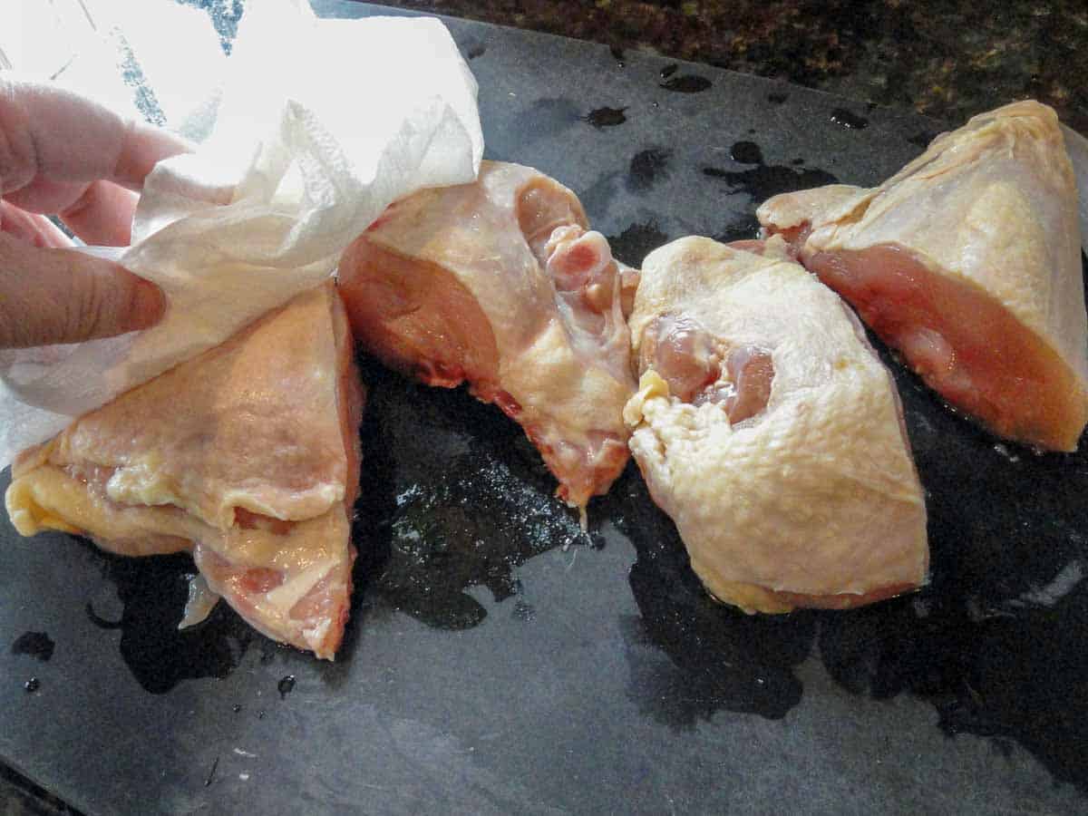 trimmed and cut up skin on chicken breasts being patted with paper towel.