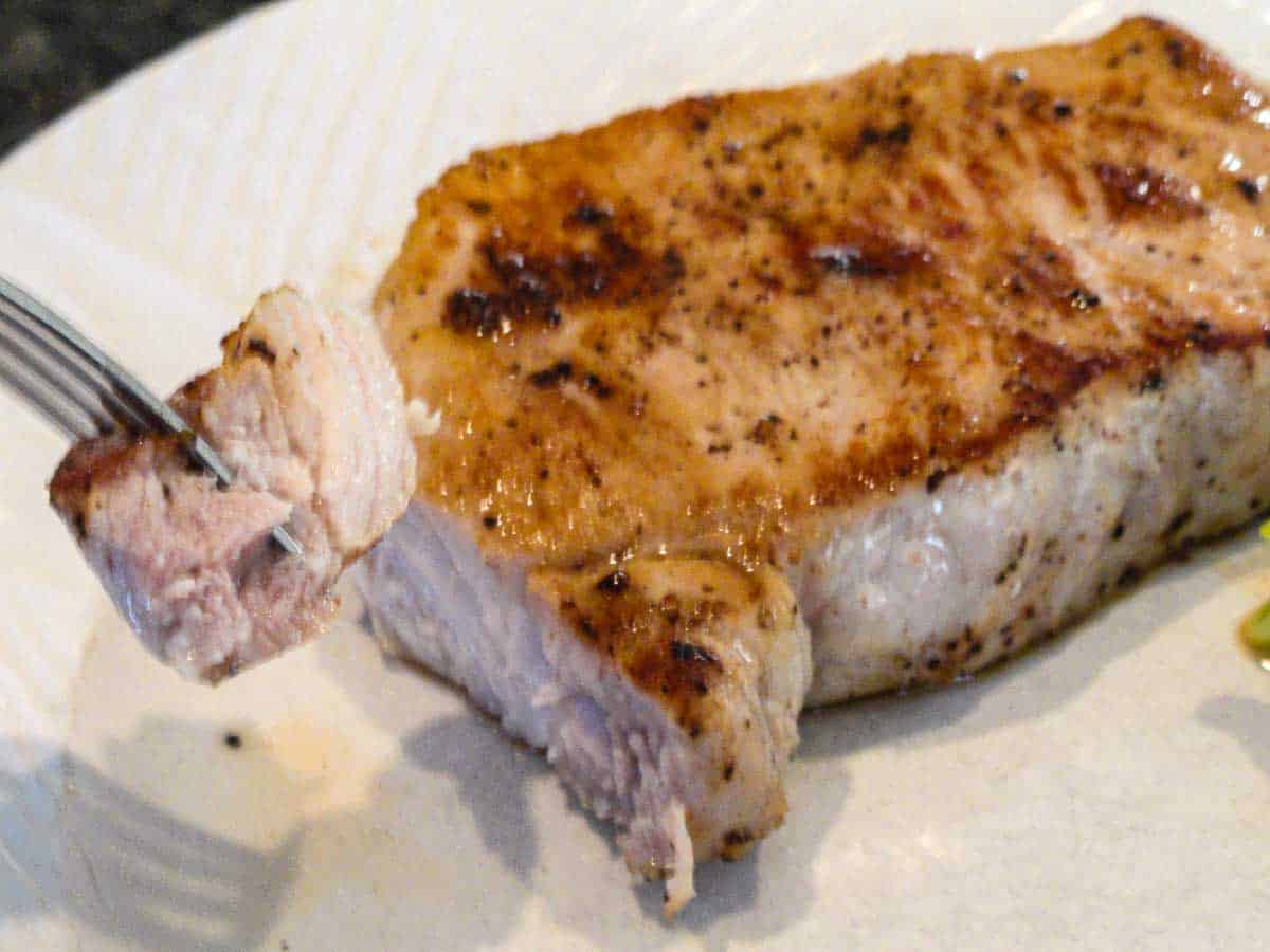 bite of pork on a fork with the chop in the background