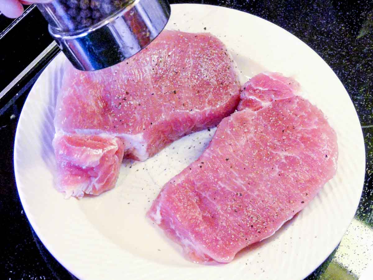 two pork chops on white plate under a pepper shaker