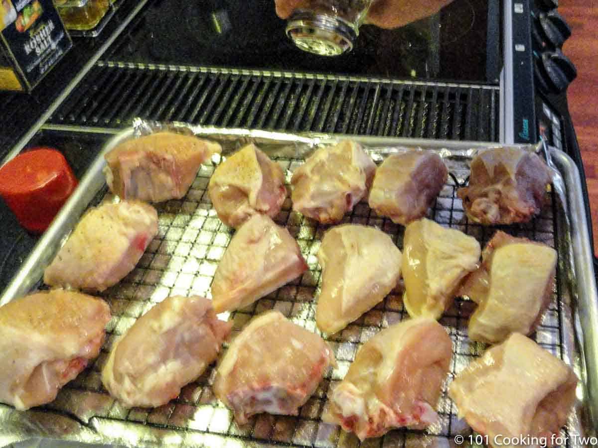 Chunks of chicken breasts on a tray being seasoned.
