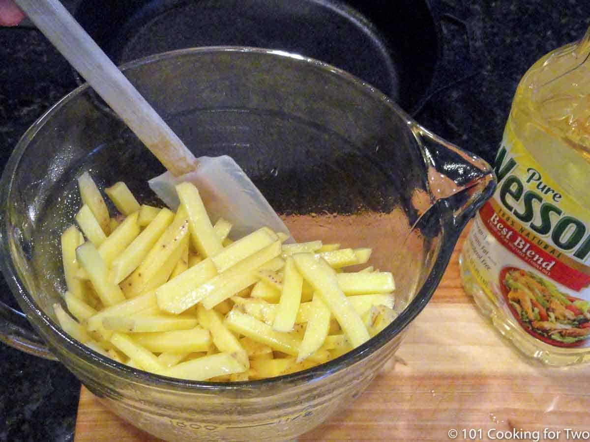 mix fries with oil in a white bowl