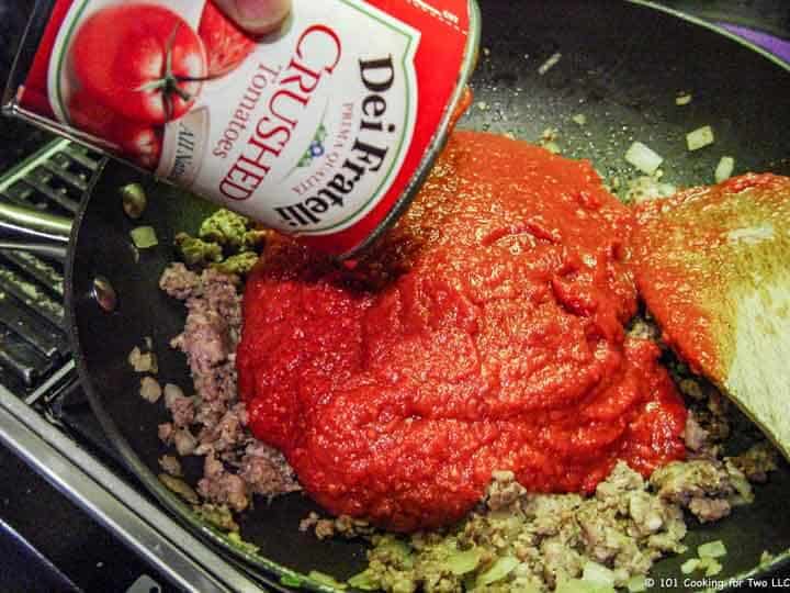 adding crushed tomatoes to cooked sausage.