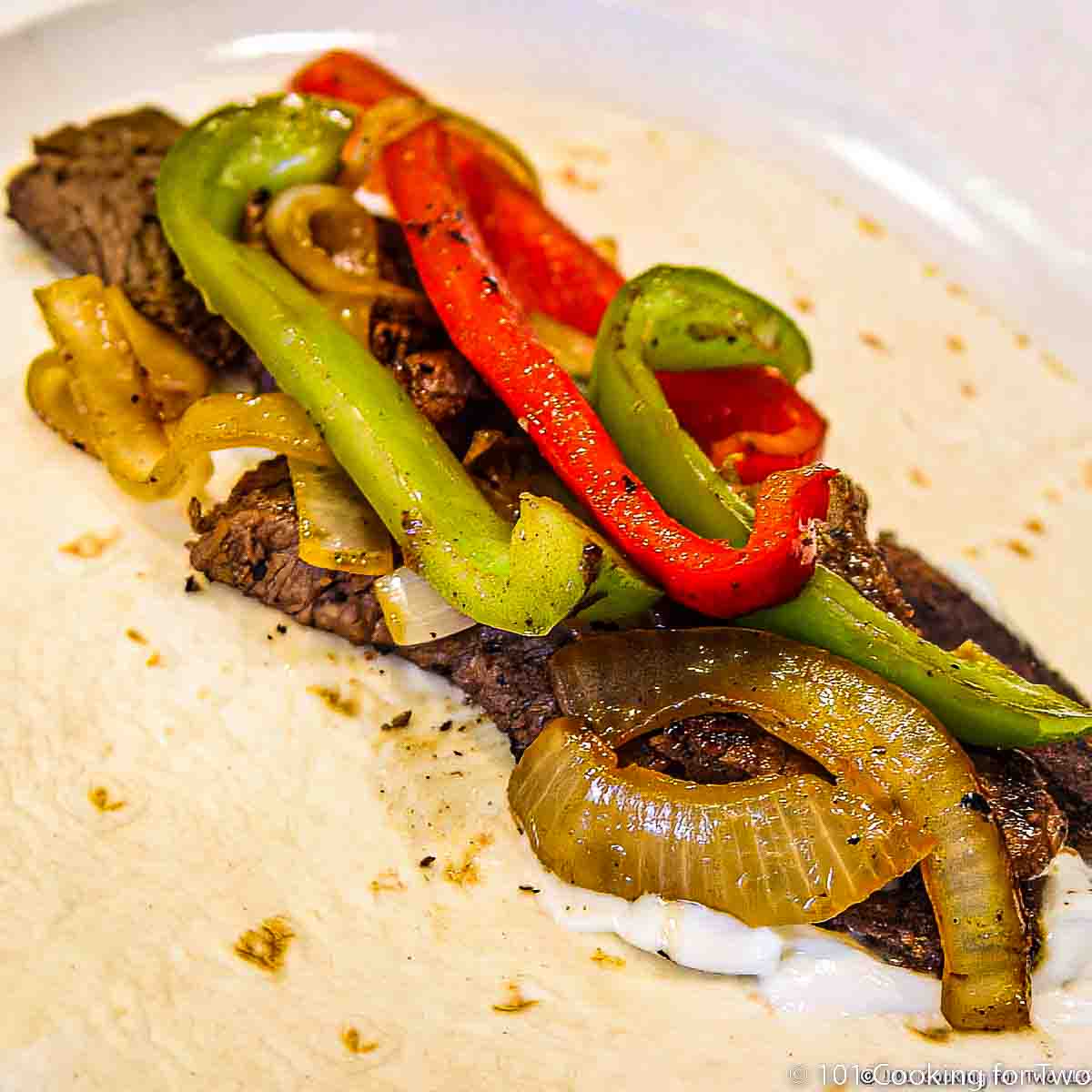 Beef Fajitas on tortilla and white plate.