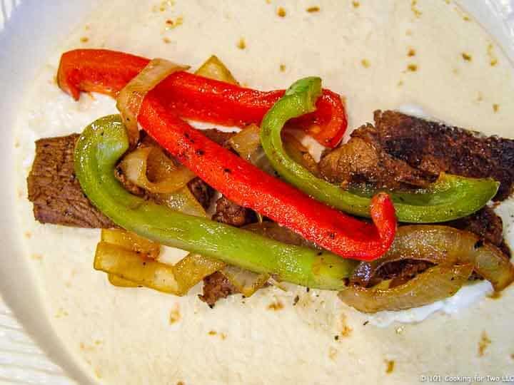 Beef Fajitas on tortilla and white plate.