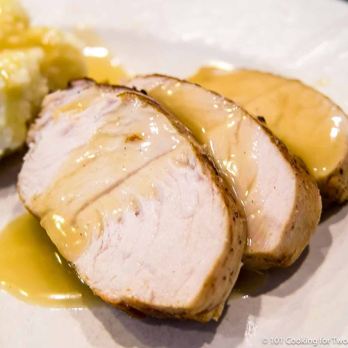 cut turkey tenderloin with gravy on plate.