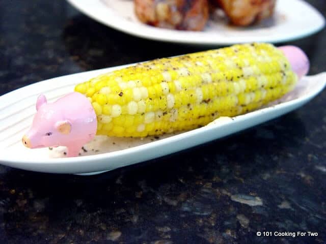 image of corn on a cob in a white tray with piggie corn holders and pepper