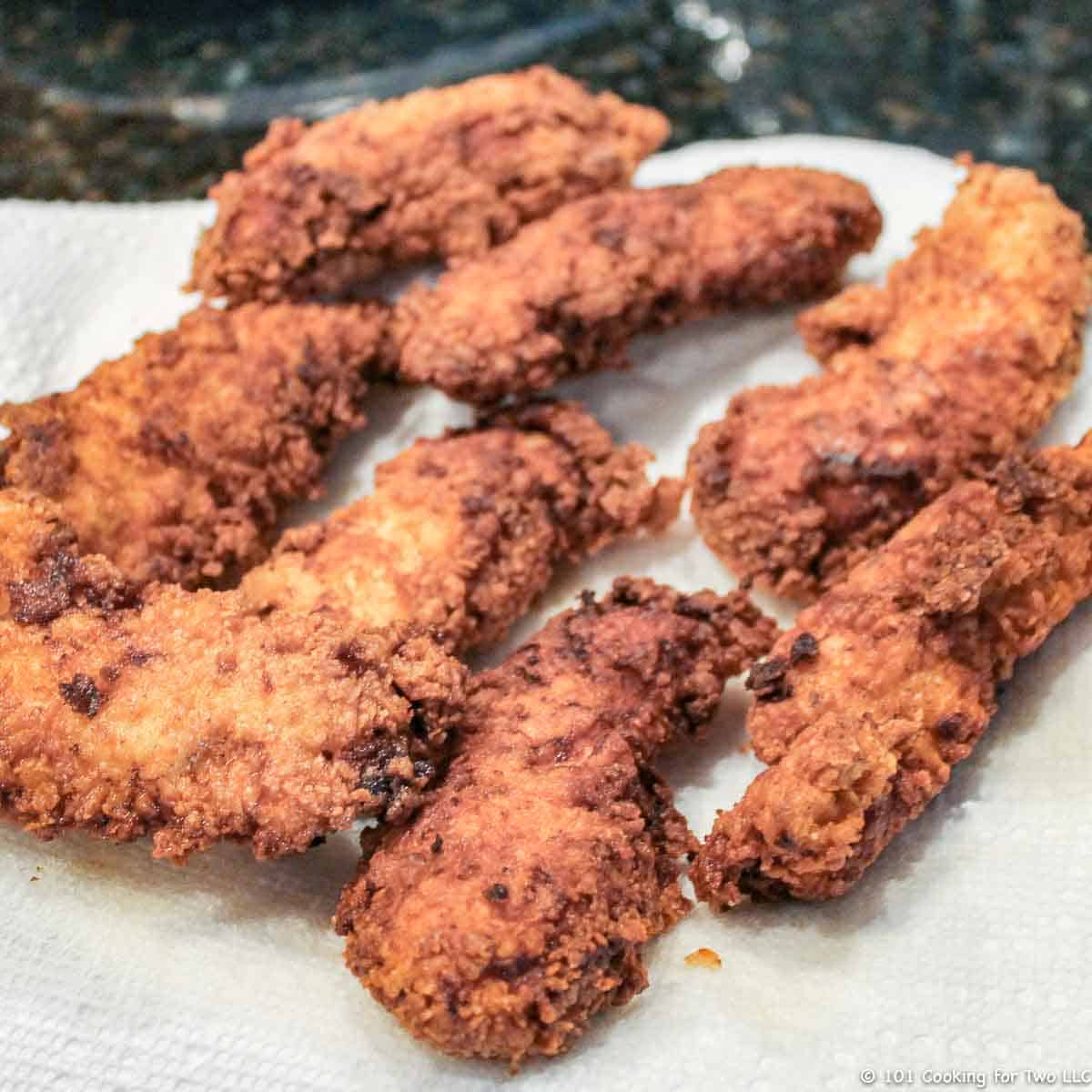 fried chicken tenders draining on a white paper towel