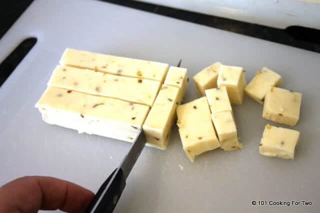 image of cutting the pepper jack cheese into cubes on a white cutting board