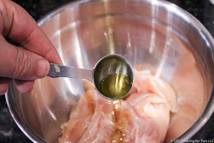 adding oil to raw chicken tenders in metal bowl