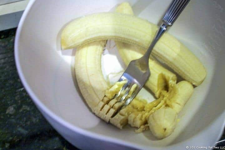 mashing 3 bananas in white bowl.