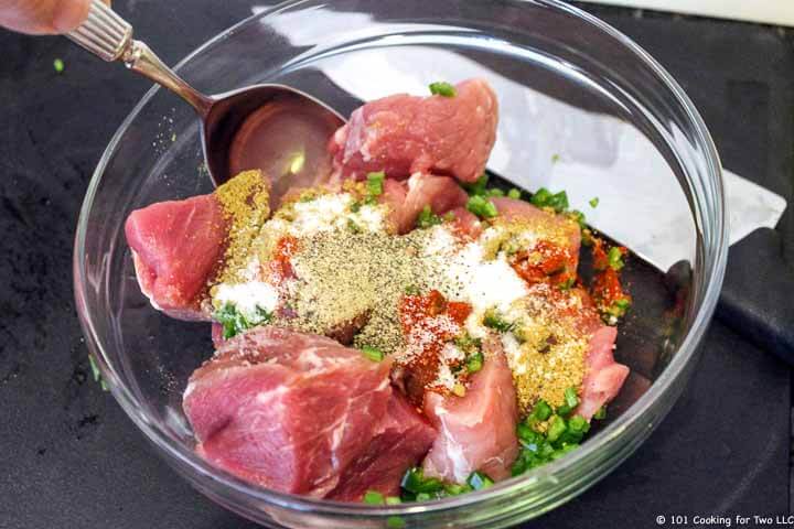 Mixing cubes of tenderlion with spices in clear bowl.