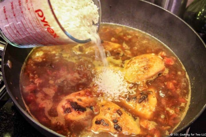 adding rice to skillet with chicken and liquid