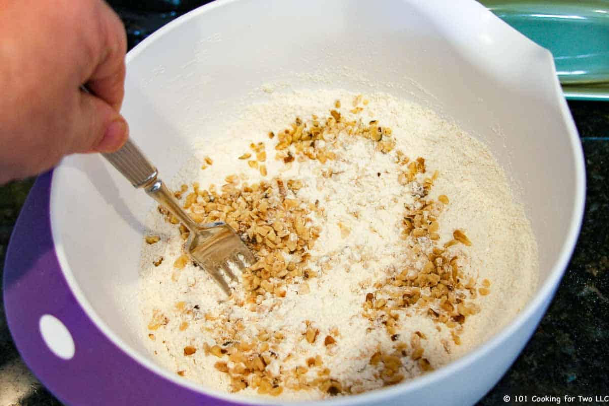 mixing nuts into dry ingreditnes in white bowl.