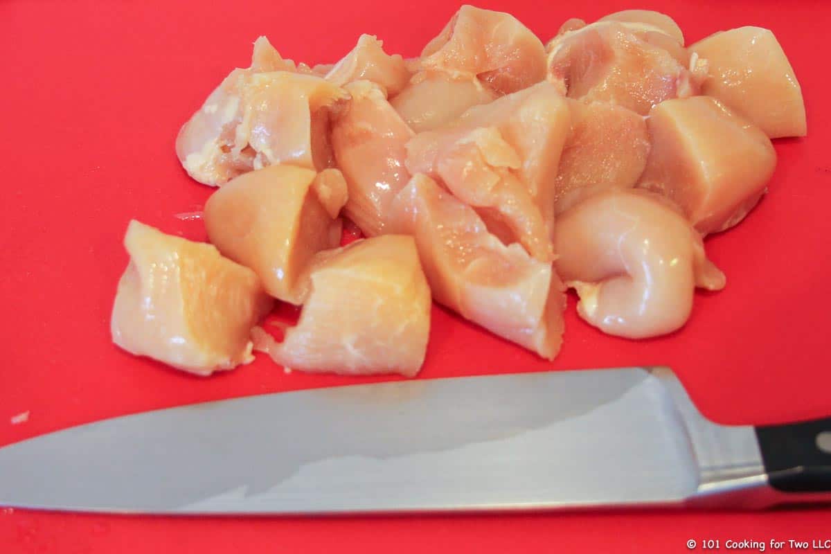 chicken cut into cubes on red board.