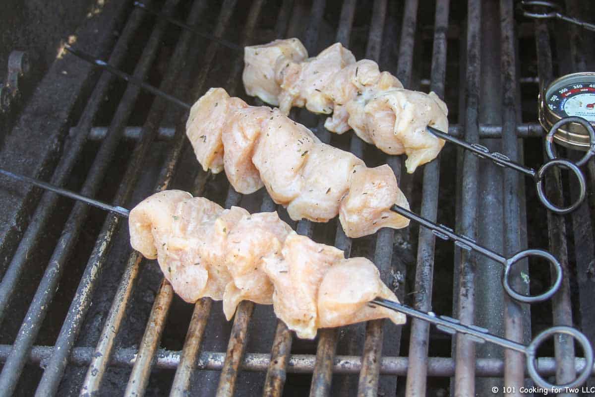 raw chicken on skewers on grill.