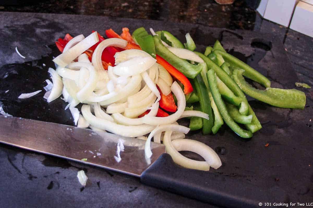 sliced peppers and onion on black board.