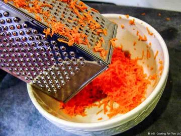 grating carrots into white bowl