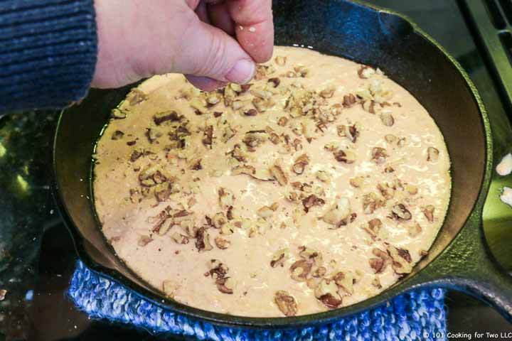 raw pancake in skillet with hand adding chopped nuts.