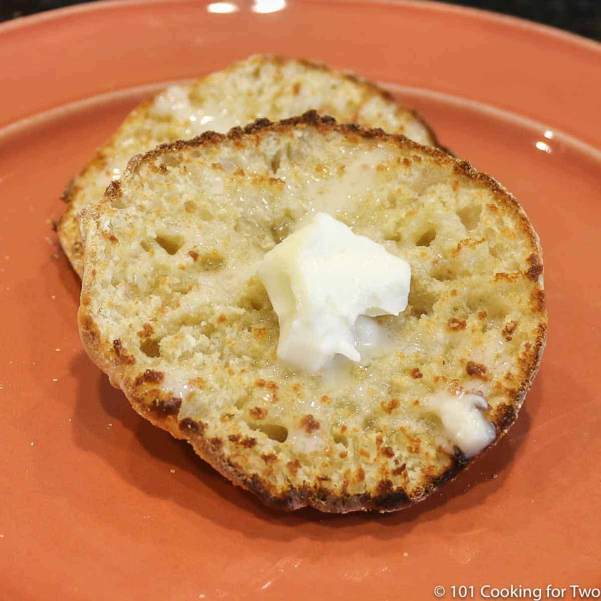English Muffin on orange plate with butter.