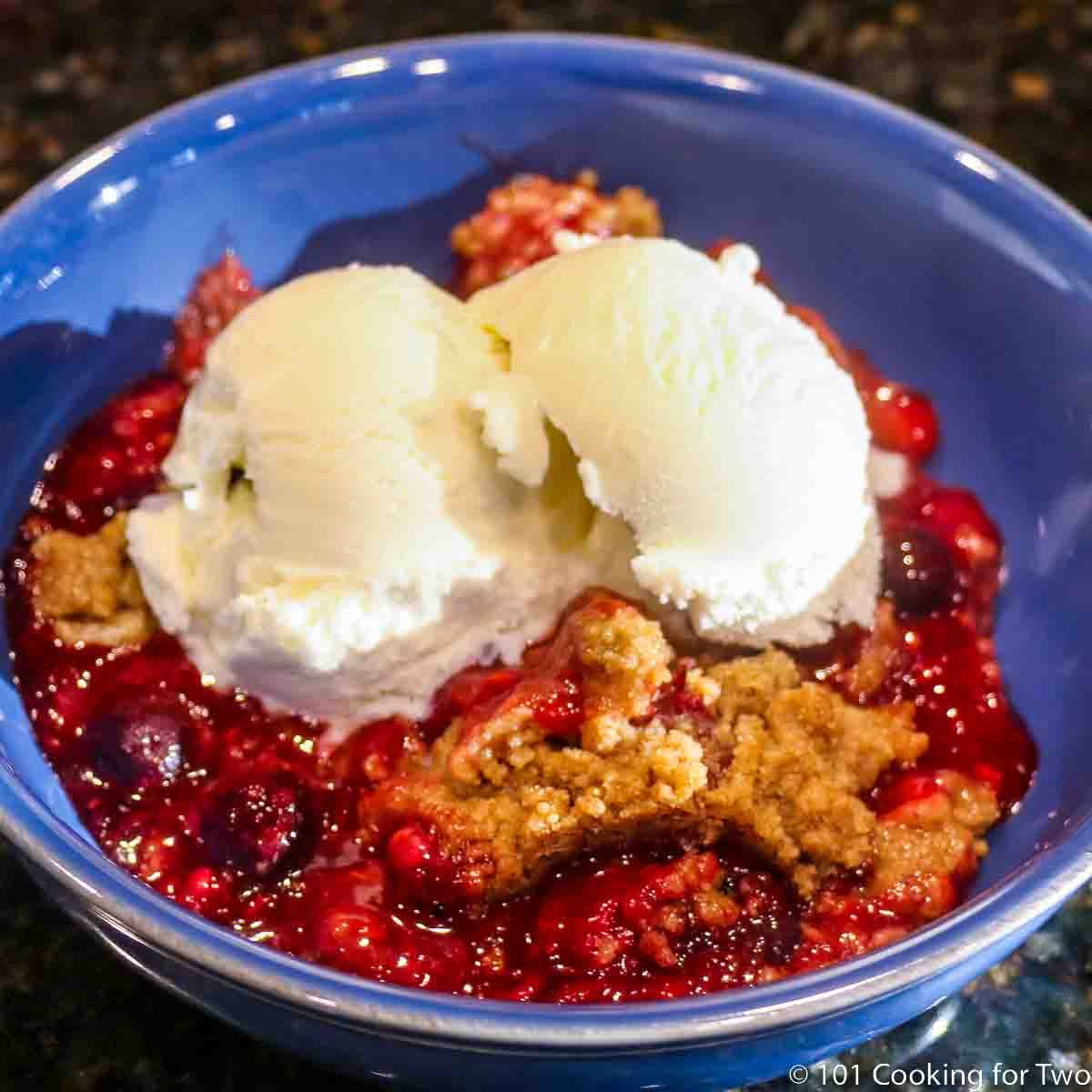 blue bowl of apple berry crumble with ice cream.