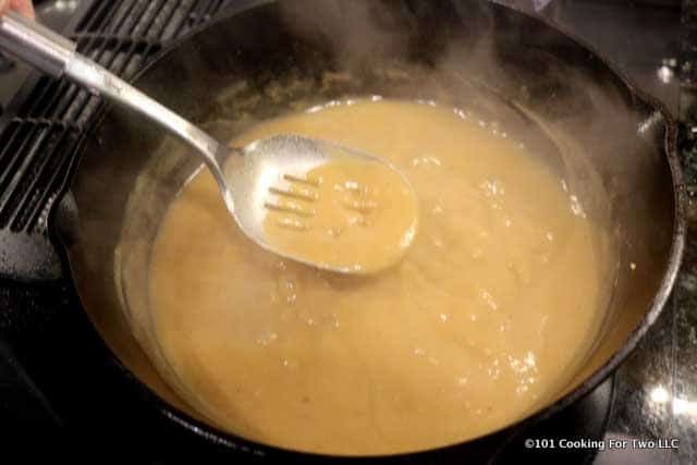 image of stirring gravy in the black pan with a slotted spoon