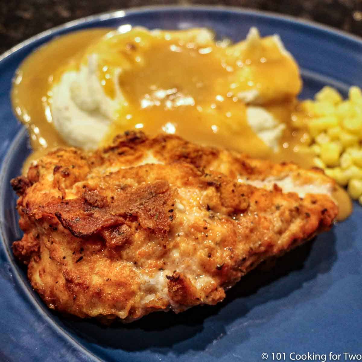 closeup image of fricd chicken with potatoes and gravy on blue plate