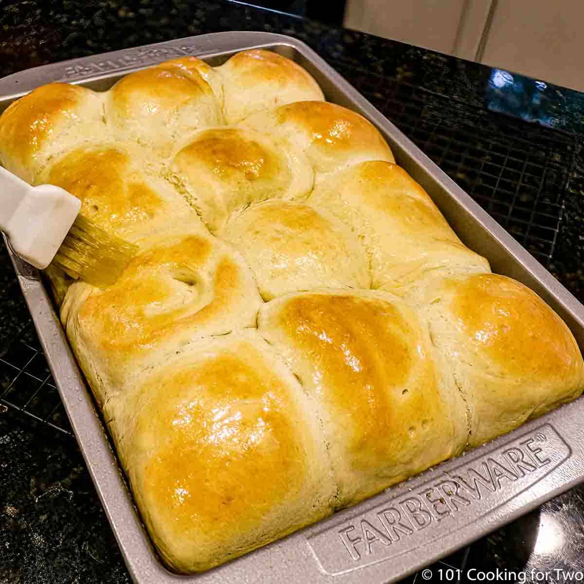 nicely browned dinner rolls still in a baking pan being brushed.