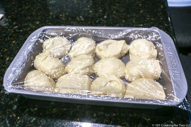 image of uncooked rolls in a baking pan with clear plastic wrap over it.