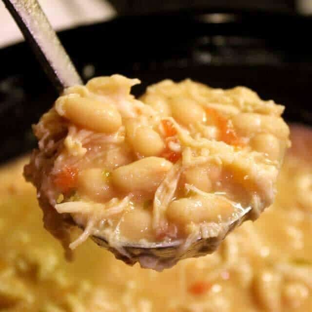 image of a ladle of cooked chicken chili over the full blace crock pot