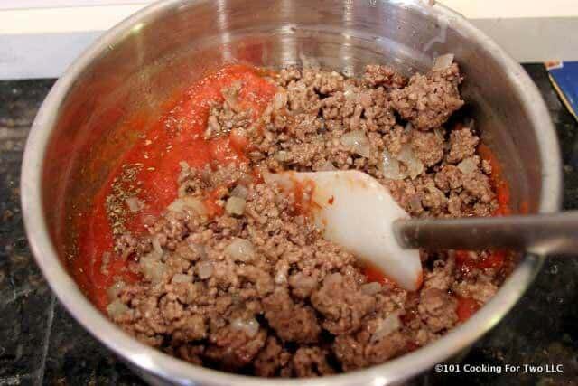 image of adding meat to sauce in a metal bowl