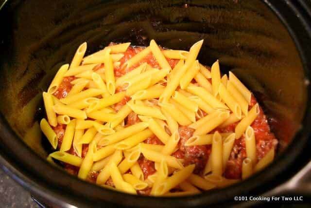 image of dry pasta being added to a layer in the crock pot