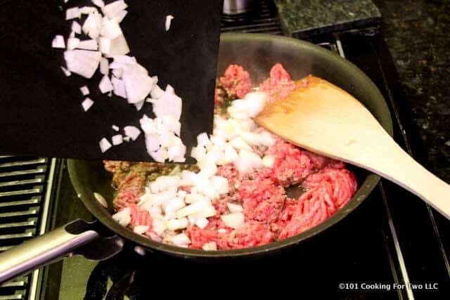 image of adding chopped onion to a frying pan of cooking meat