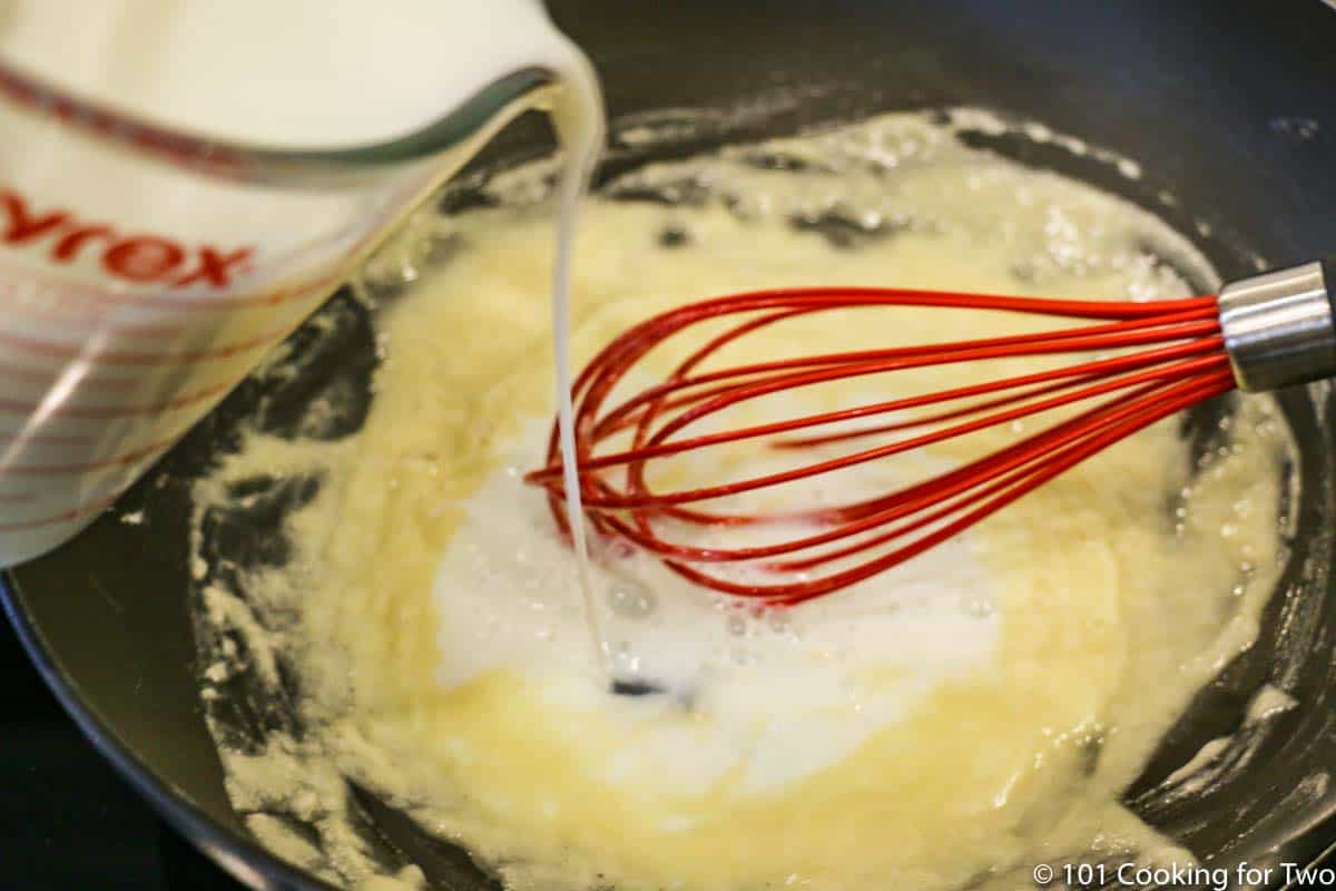 whisking milk into roux in pan.