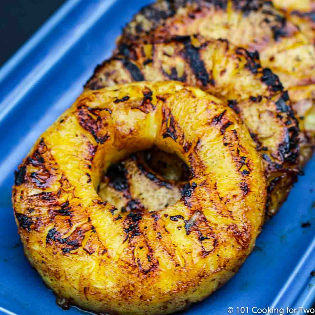 Grilled Pineapple from 101 Cooking for Two close up of Grilled Pineacpple with grill marks on a blue plate.