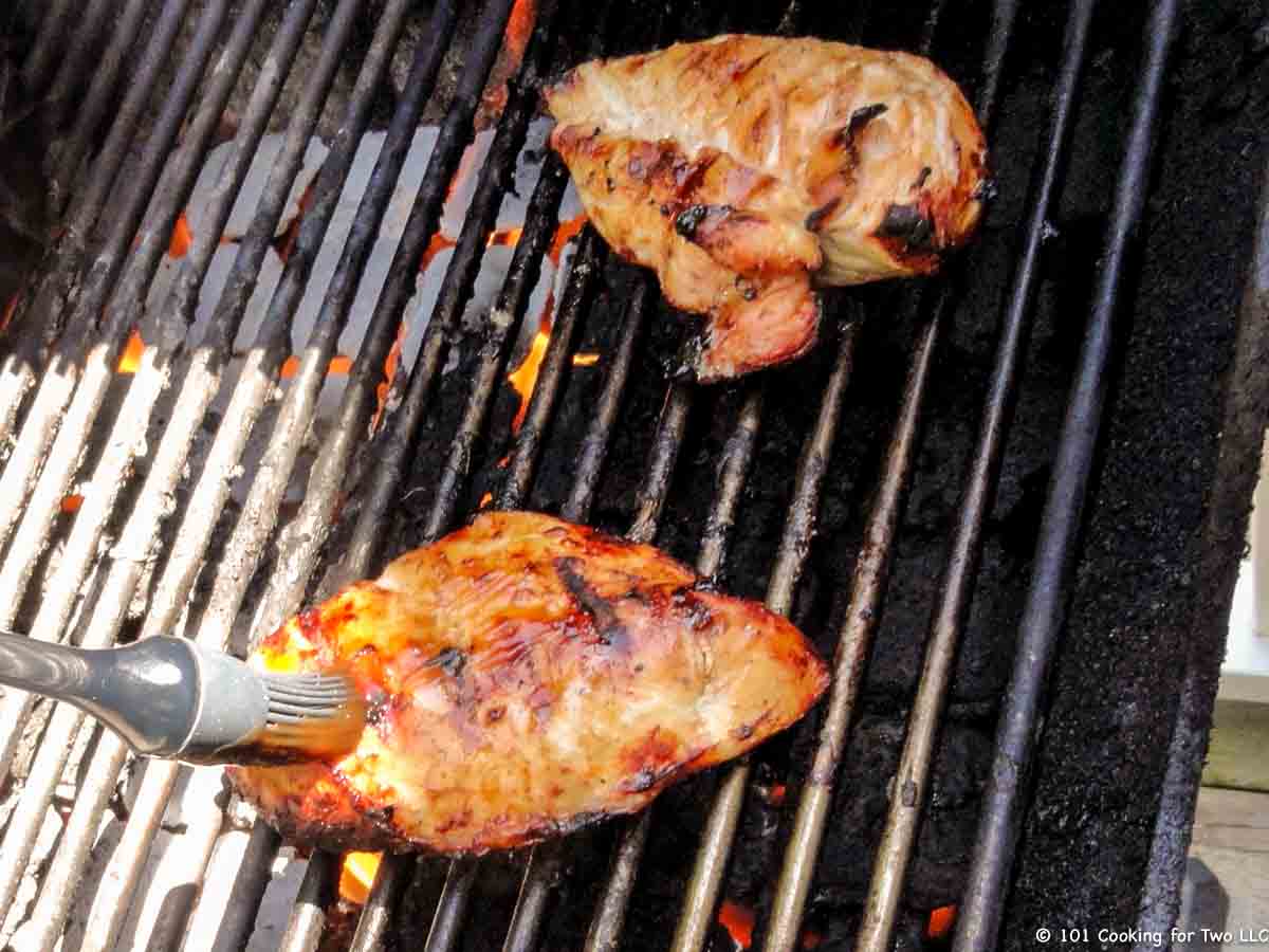 brushing chicken with sauce on the grill.