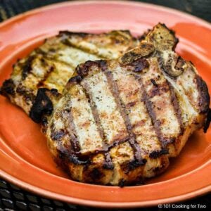 Two grilled pork chops on an orange plate.