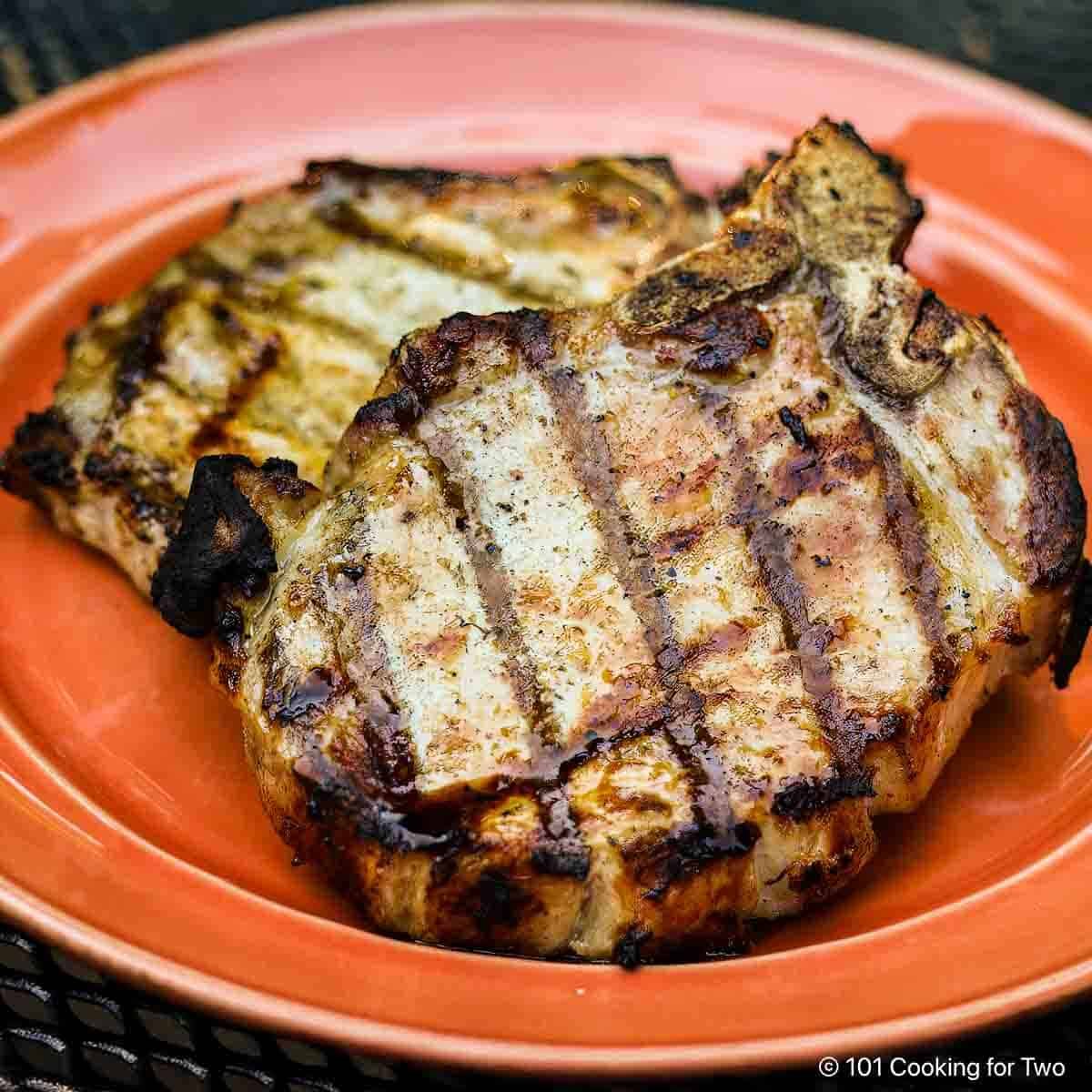 Close up picture of two grilled pork chops on orange plate